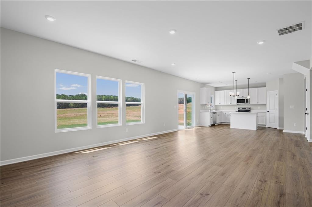 Open-concept living space featuring wood-finish flooring, recessed lighting, and a white kitchen with an island, pendant lighting, and stainless steel appliances