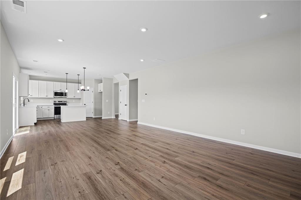Open-concept living area with wood-finish flooring, recessed lighting, and a kitchen featuring white cabinetry and a central island