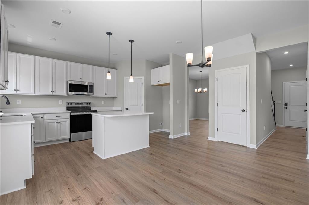 Modern kitchen featuring white cabinetry, stainless steel appliances, a center island, pendant lighting, and wood-finish flooring