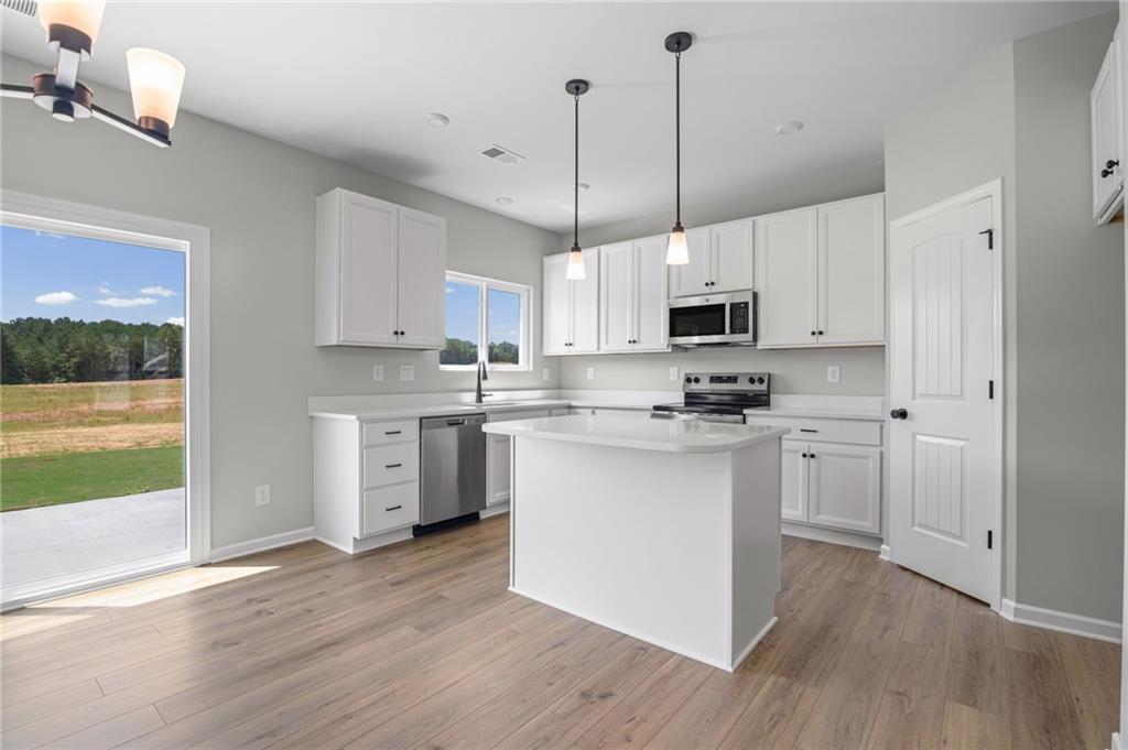 Kitchen featuring white cabinetry, stainless steel appliances, a center island with countertop, wood-finish flooring, and pendant lighting