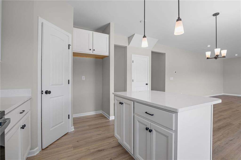 Kitchen island with a white countertop and white cabinetry, wood-finish flooring, and pendant lighting