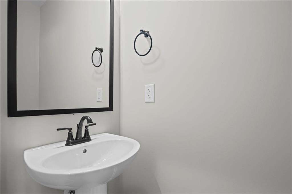 Pedestal sink with a matte black faucet, framed mirror, and a wall-mounted towel ring