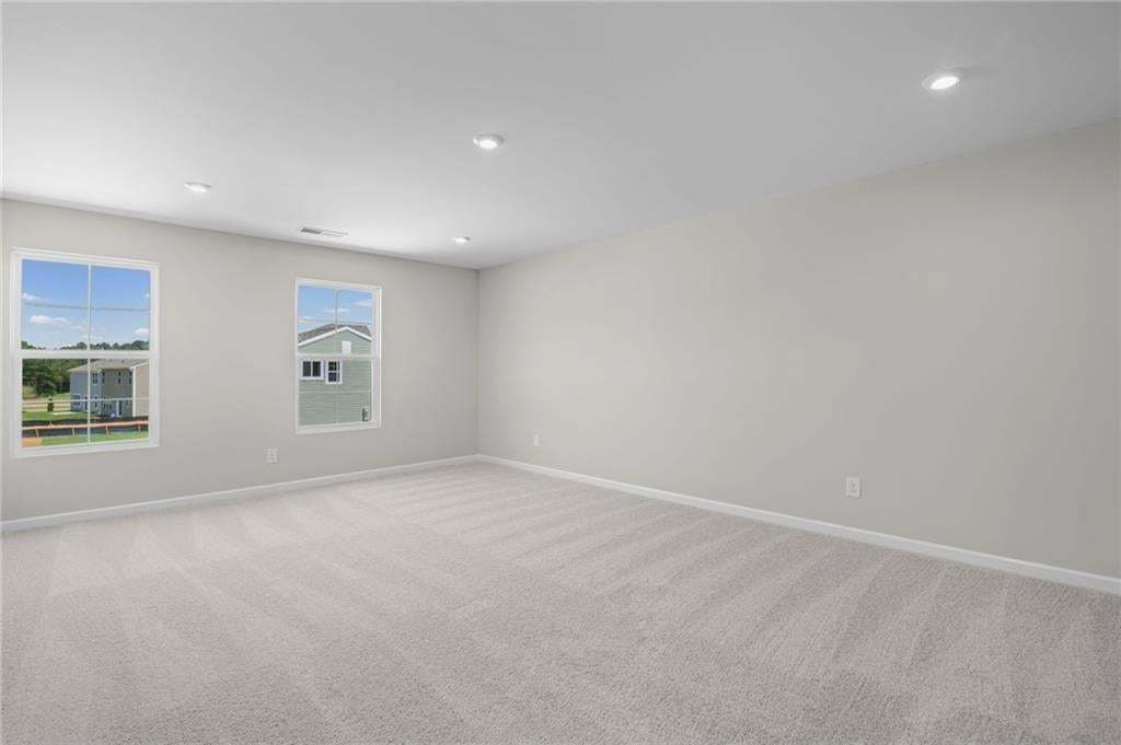 Expansive room with neutral carpeting, recessed lighting, and multiple windows providing ambient light