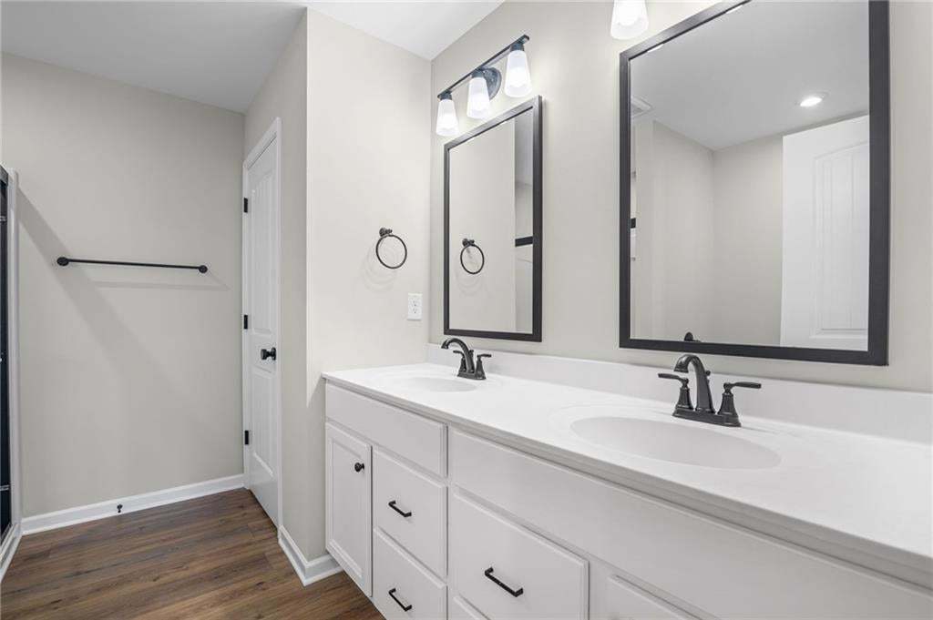 Double vanity with matte black fixtures and framed mirrors, white shaker cabinetry, and wood-finish flooring