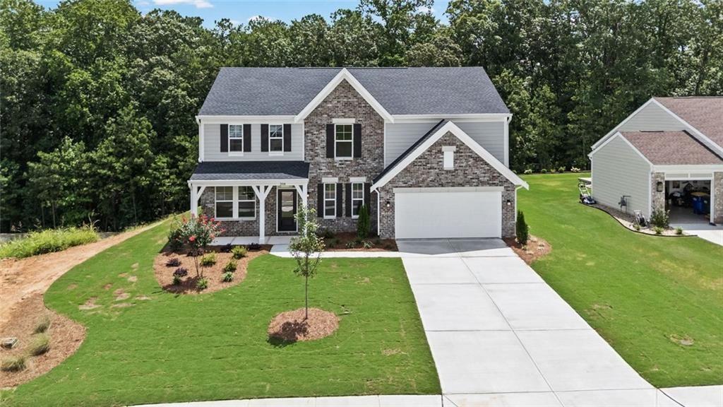 Two-story property featuring a stone and siding exterior, a dark shingle roof, a covered entry porch with white columns, a two-car garage, and a concrete driveway