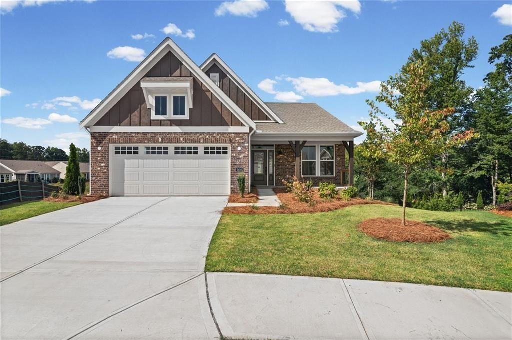 Craftsman-style home featuring a brick and shake exterior, a two-car garage with transom windows, a concrete driveway, a covered front porch with timber posts, and mature landscaping