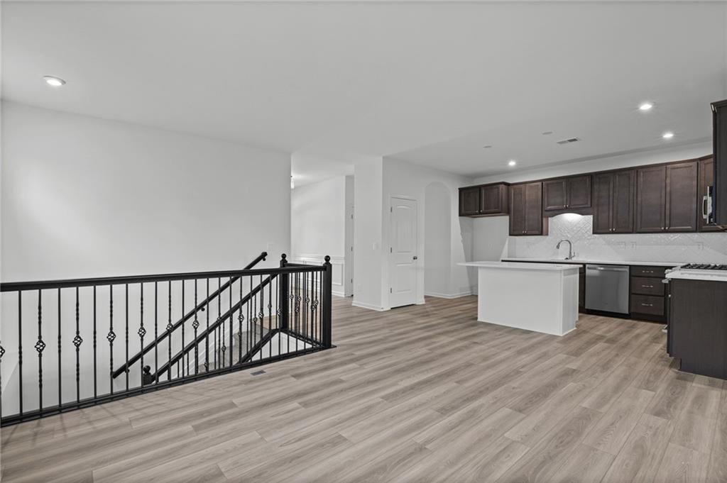 Open-concept living space featuring wood-finish flooring, recessed lighting, and a kitchen with dark cabinetry, stainless steel appliances, and a central island