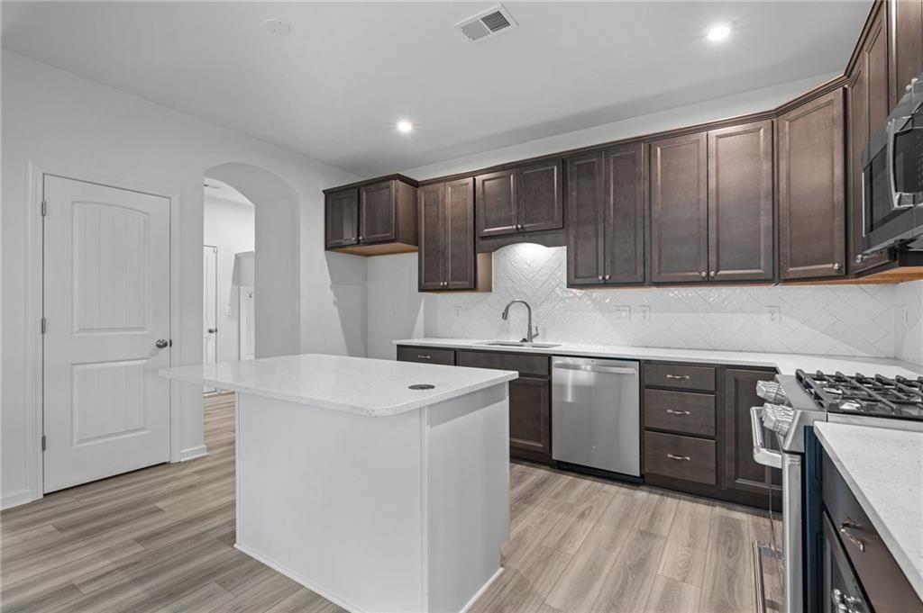 Kitchen featuring a central island with white countertop, dark wood-finish cabinetry, stainless steel appliances, and wood-finish flooring