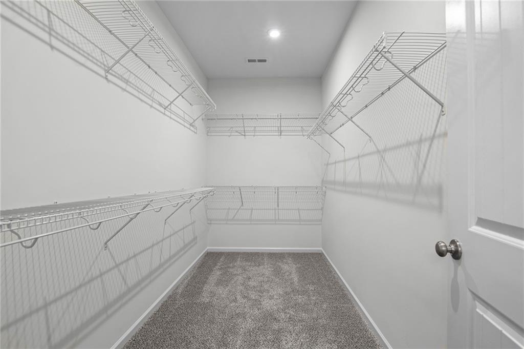Walk-in closet featuring built-in wire shelving, plush gray carpeting, recessed ceiling lighting, and a paneled interior door with a brushed nickel knob