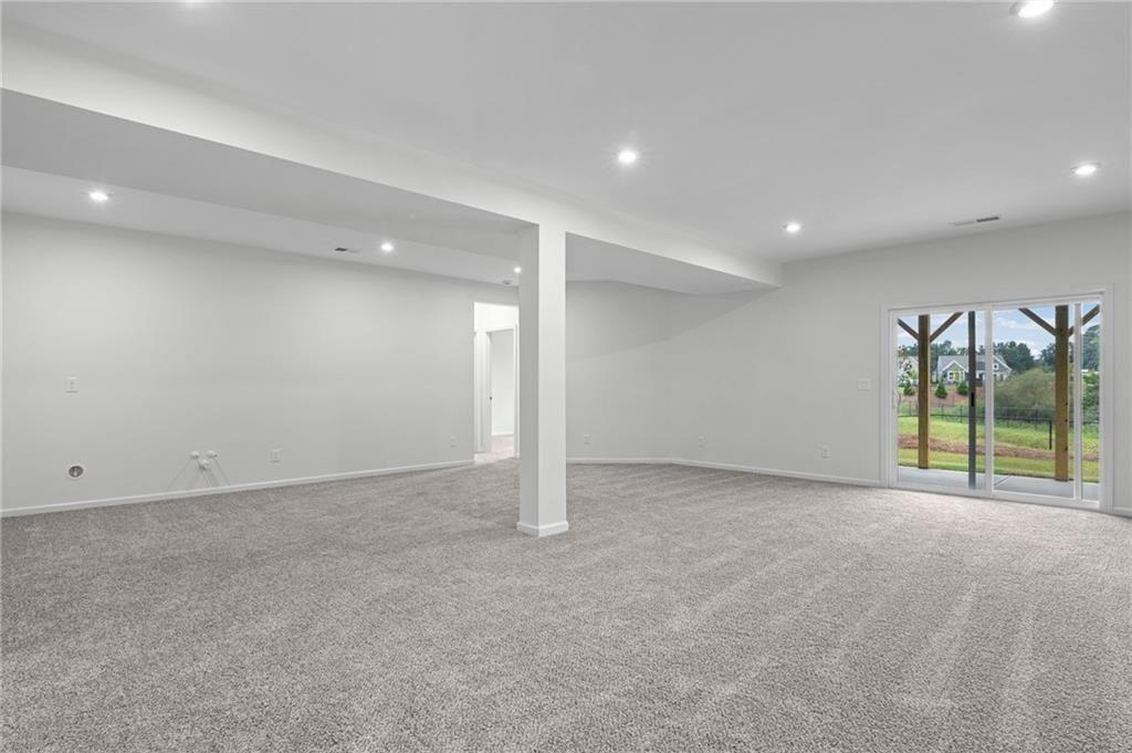 Spacious lower-level room featuring light gray carpeting, recessed lighting, and a sliding glass door