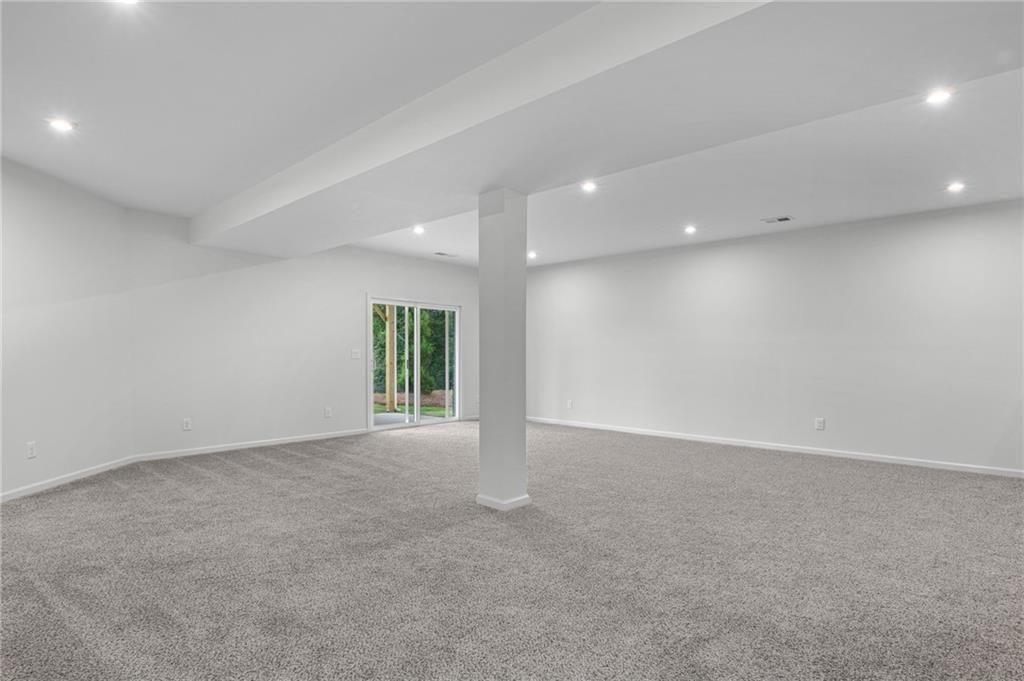 Spacious room featuring light gray carpeting, recessed ceiling lighting, a structural support column, and glass sliding doors providing exterior access