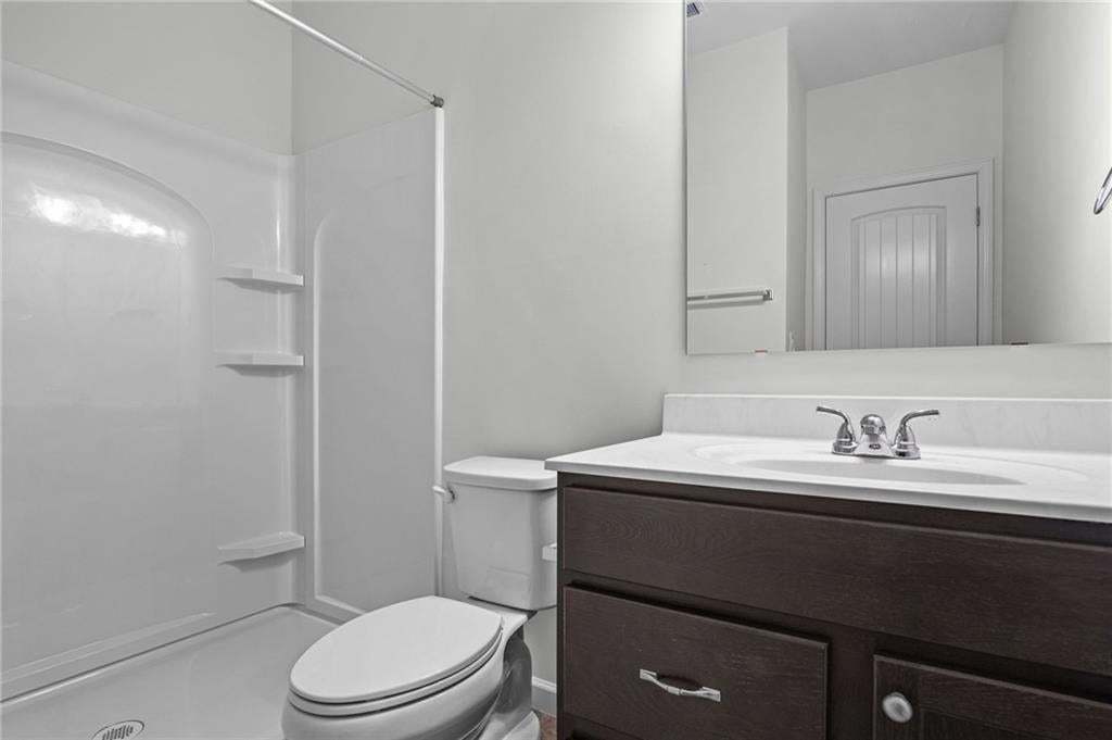 Bathroom featuring a shower stall with built-in shelving, a toilet, and a vanity with a white countertop and dark wood-finish cabinetry
