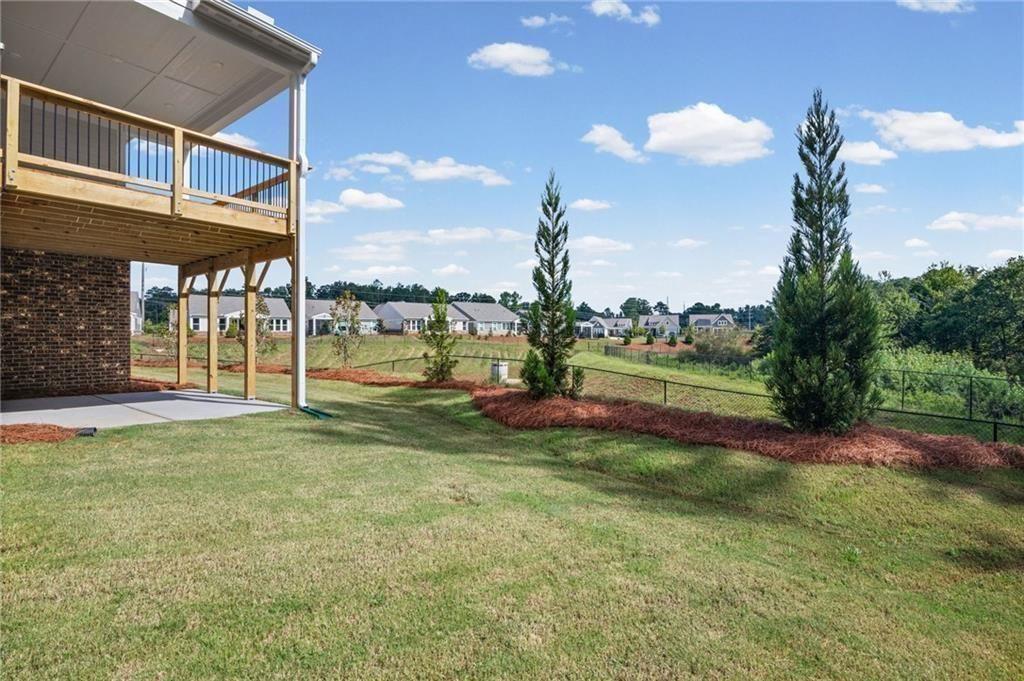 Expansive green lawn featuring a covered patio, a raised wooden deck with railings, and established ornamental trees