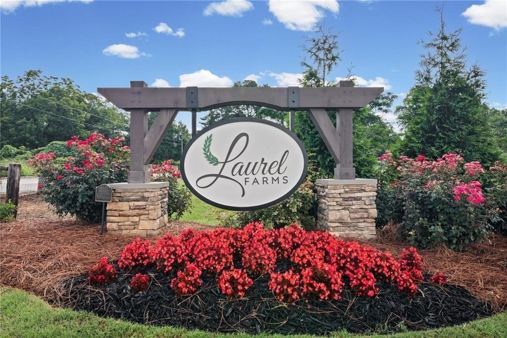 Community entrance sign featuring a dark wood pergola with stone-clad pillars, vibrant red and pink flowering shrubs, and dark mulch landscaping