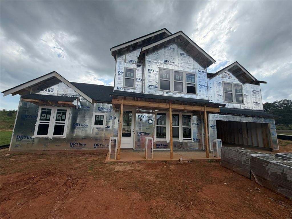 Two-story home under construction featuring a covered front porch with exposed wood columns, multiple windows, an attached garage, and a dark shingle roof