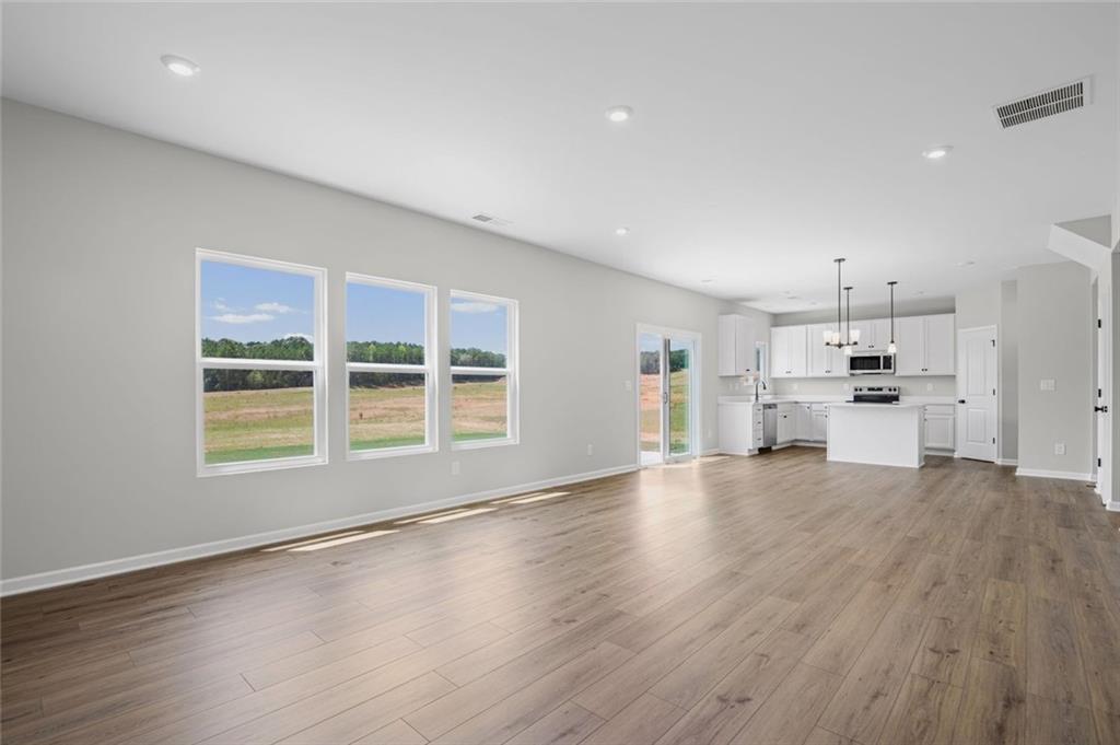 Open-concept living space featuring wood-finish flooring, recessed lighting, and a white kitchen with an island, pendant lighting, and stainless steel appliances
