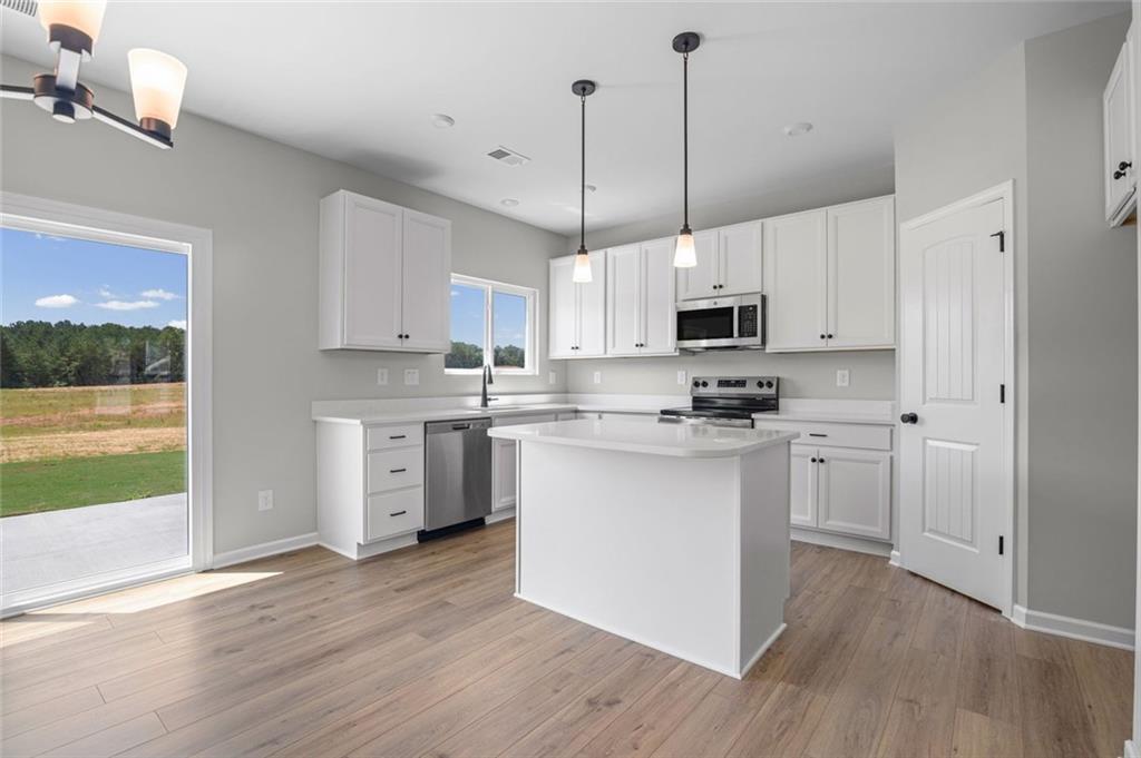 Kitchen featuring white cabinetry, stainless steel appliances, a center island with countertop, wood-finish flooring, and pendant lighting