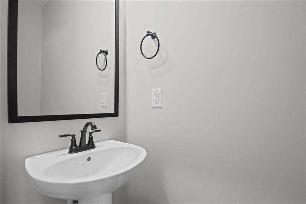 Pedestal sink with a matte black faucet, framed mirror, and a wall-mounted towel ring