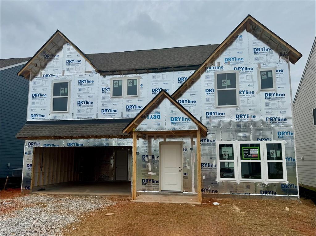 Two-story residential structure under construction featuring a dark shingled roof, multiple windows with white frames, and a prominent front entry door
