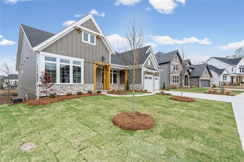 View of front of home with board and batten siding, stone siding, a front lawn, driveway, and a shingled roof