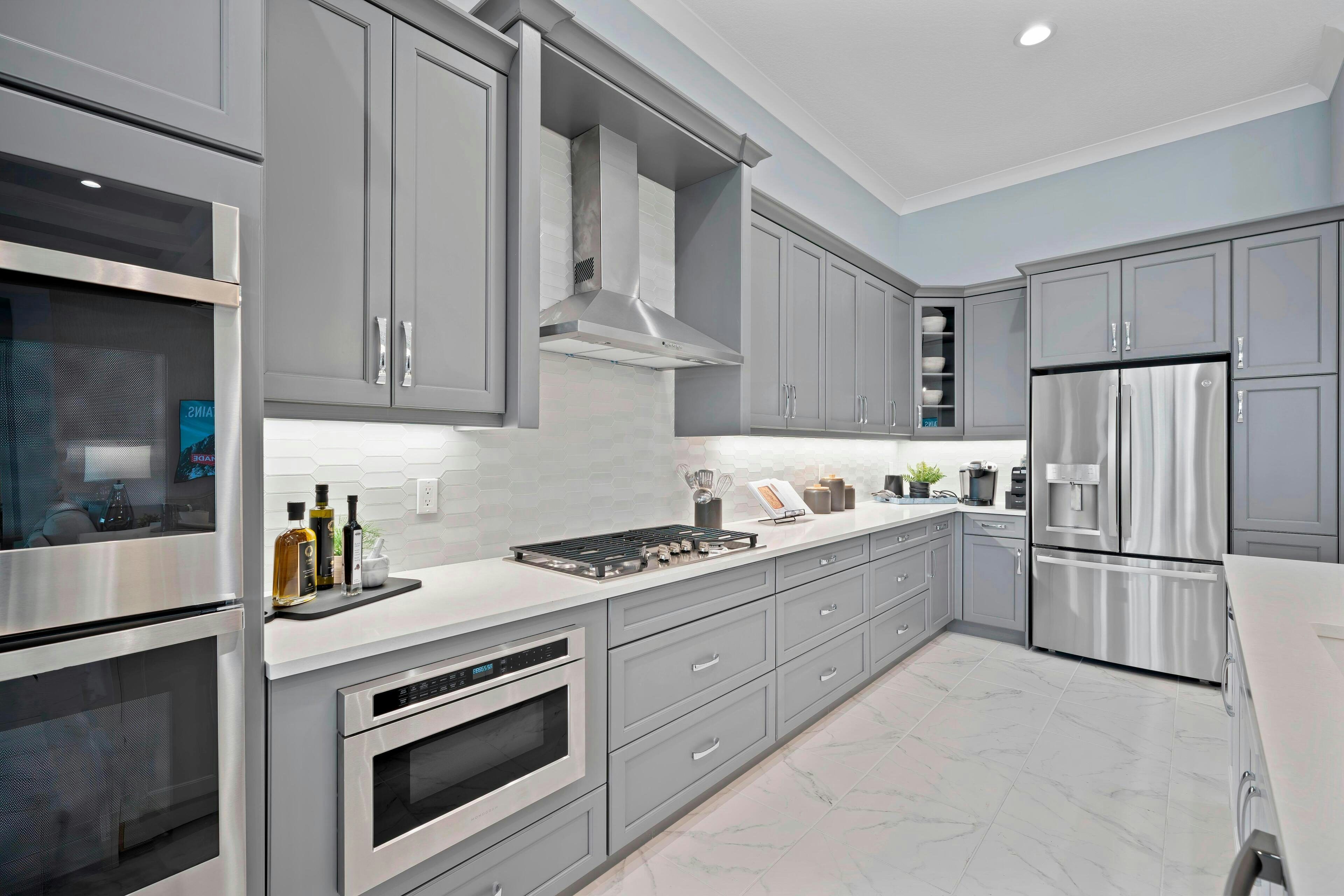 Cook wall in kitchen with grey cabinets, grey tile backsplash and stainless steel appliances