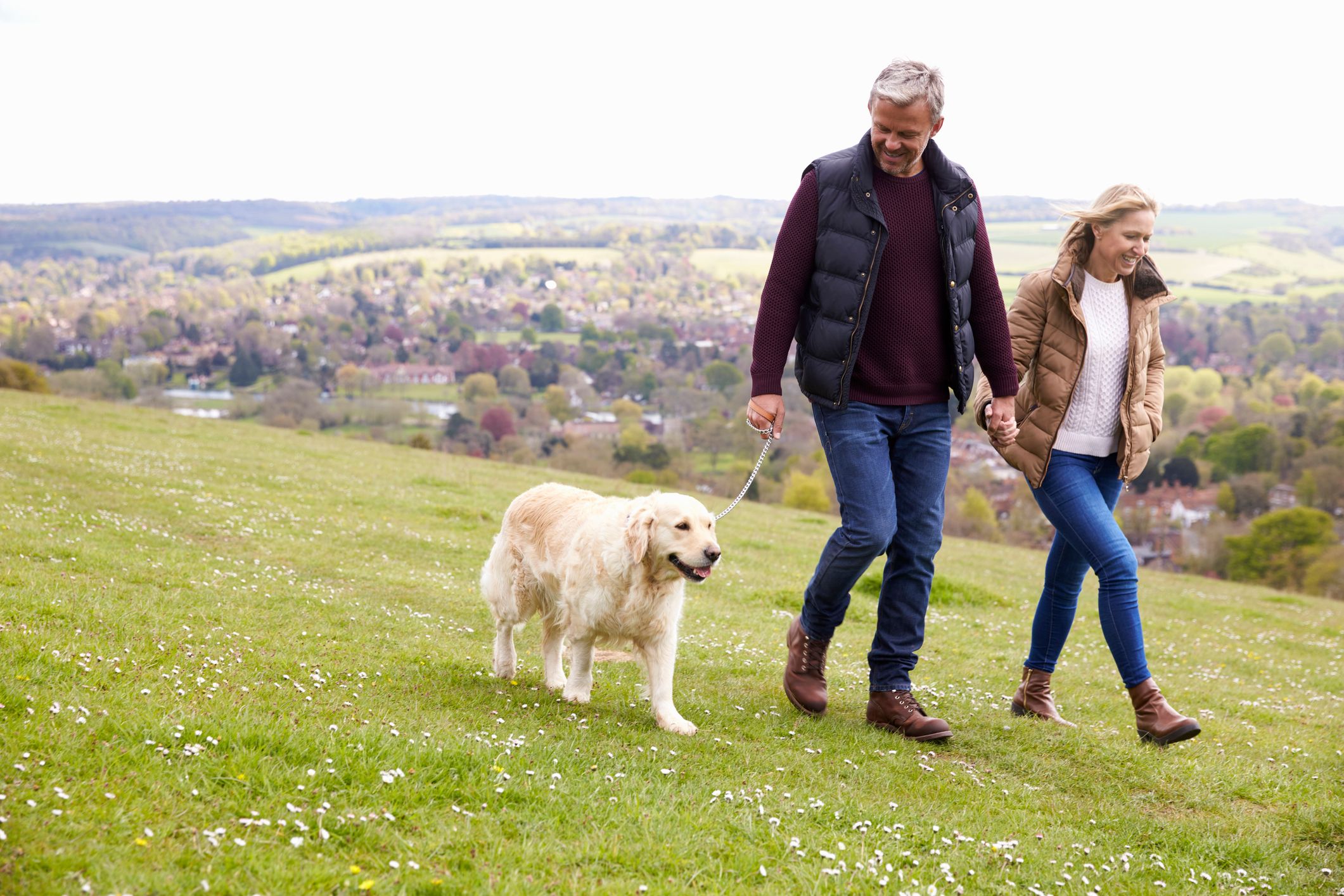 Active Adult Couple Walking a dog on a grassy hill
