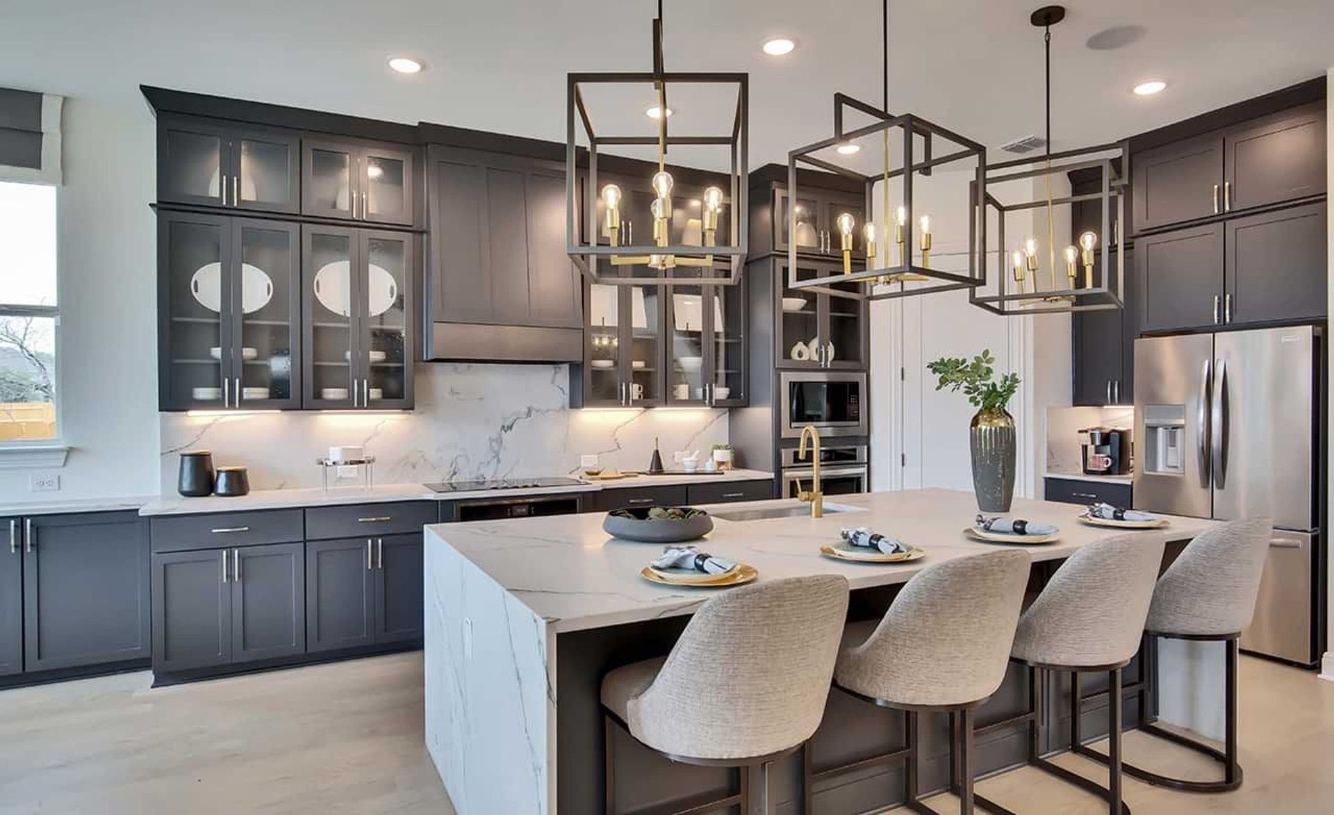 Elegant kitchen boasts marble island, modern pendant lighting, and sleek dark cabinetry. Oaks at San Gabriel.