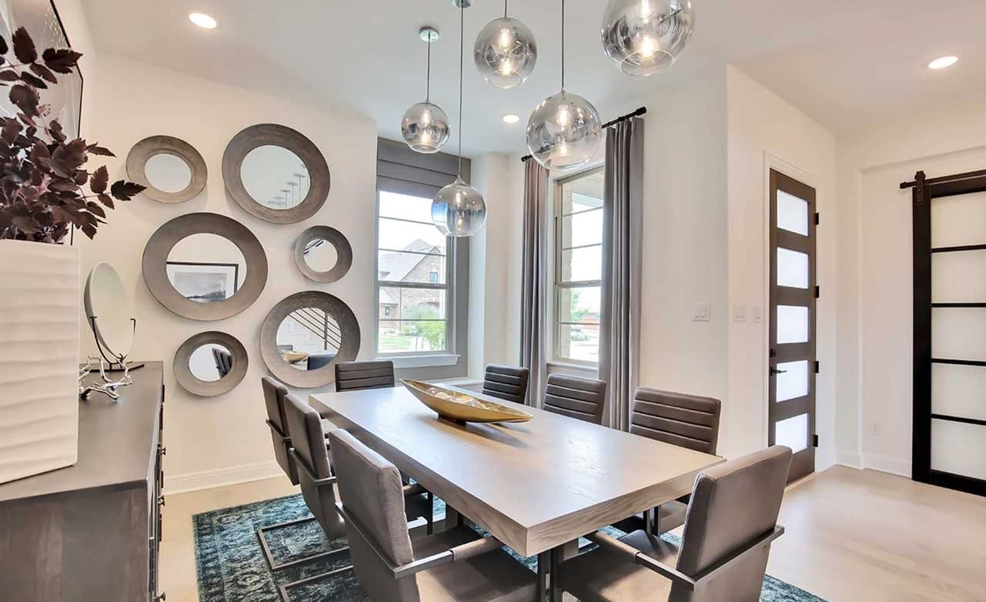Sleek round mirrors and globe lighting create modern elegance in Oaks at San Gabriel dining room.