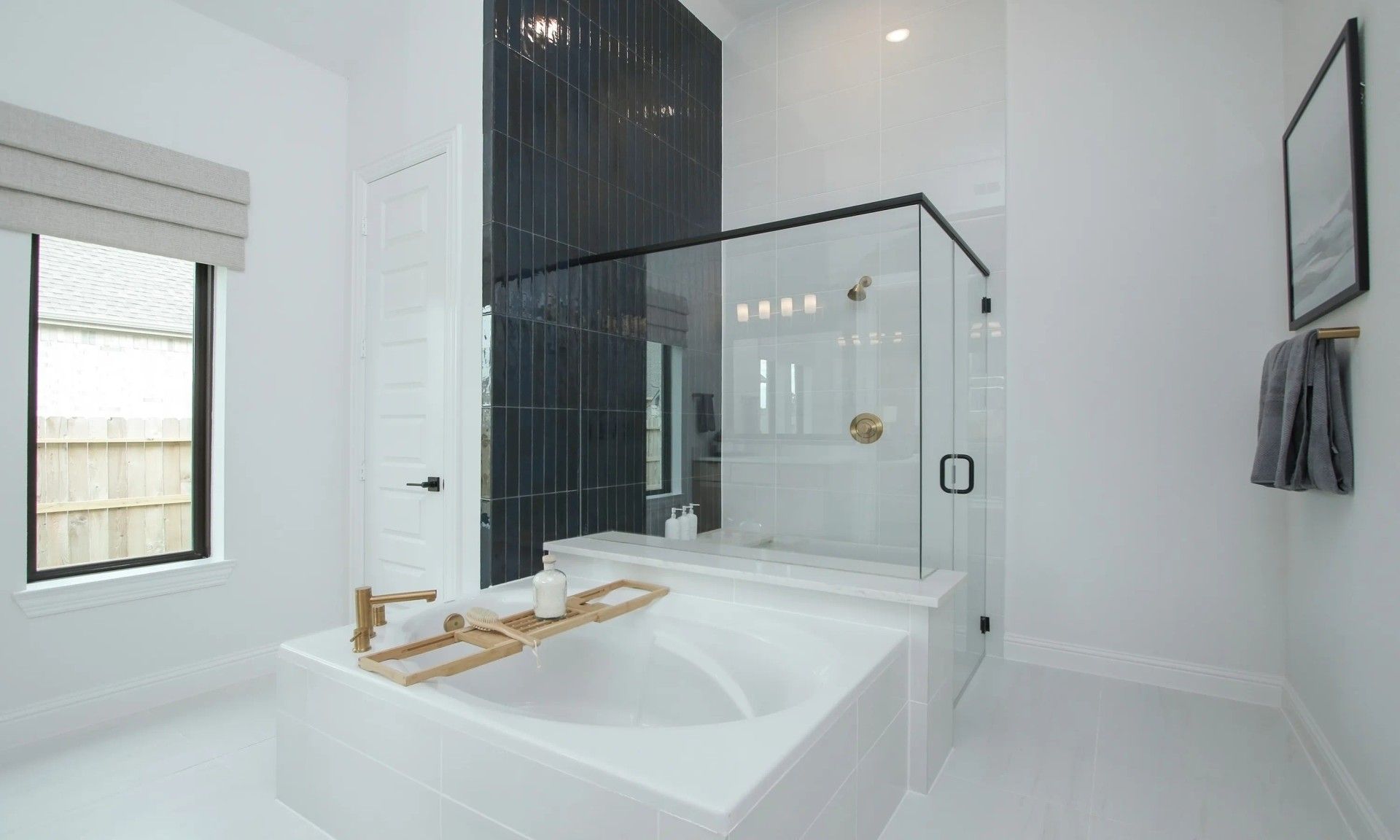 Experience elegance with a freestanding tub and gold fixtures against a striking black tile wall in Coastal Point.