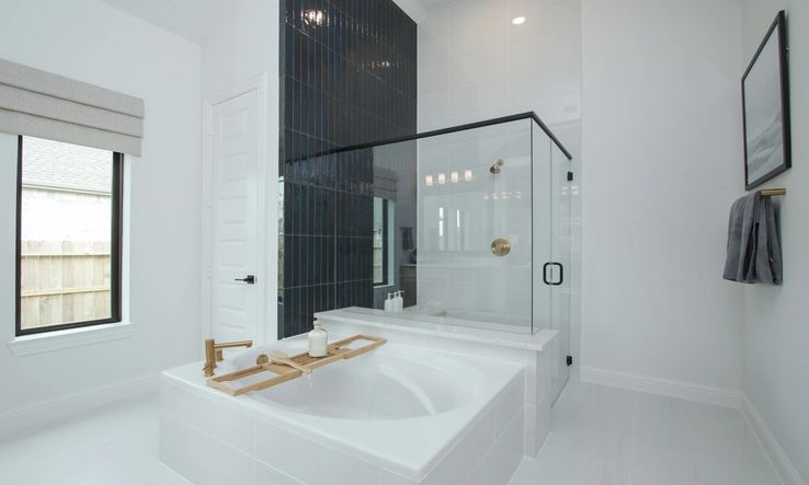 Experience elegance with a freestanding tub and gold fixtures against a striking black tile wall in Coastal Point.