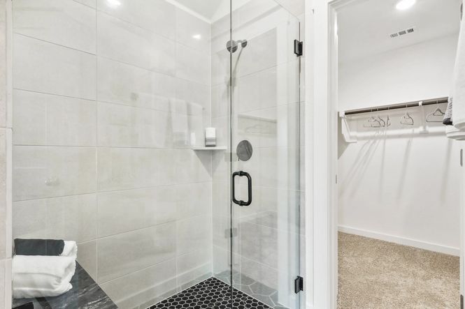 Elegant glass shower with sleek black fixtures and hexagon tile floor, adjacent to walk-in closet, Simpson Crossing.