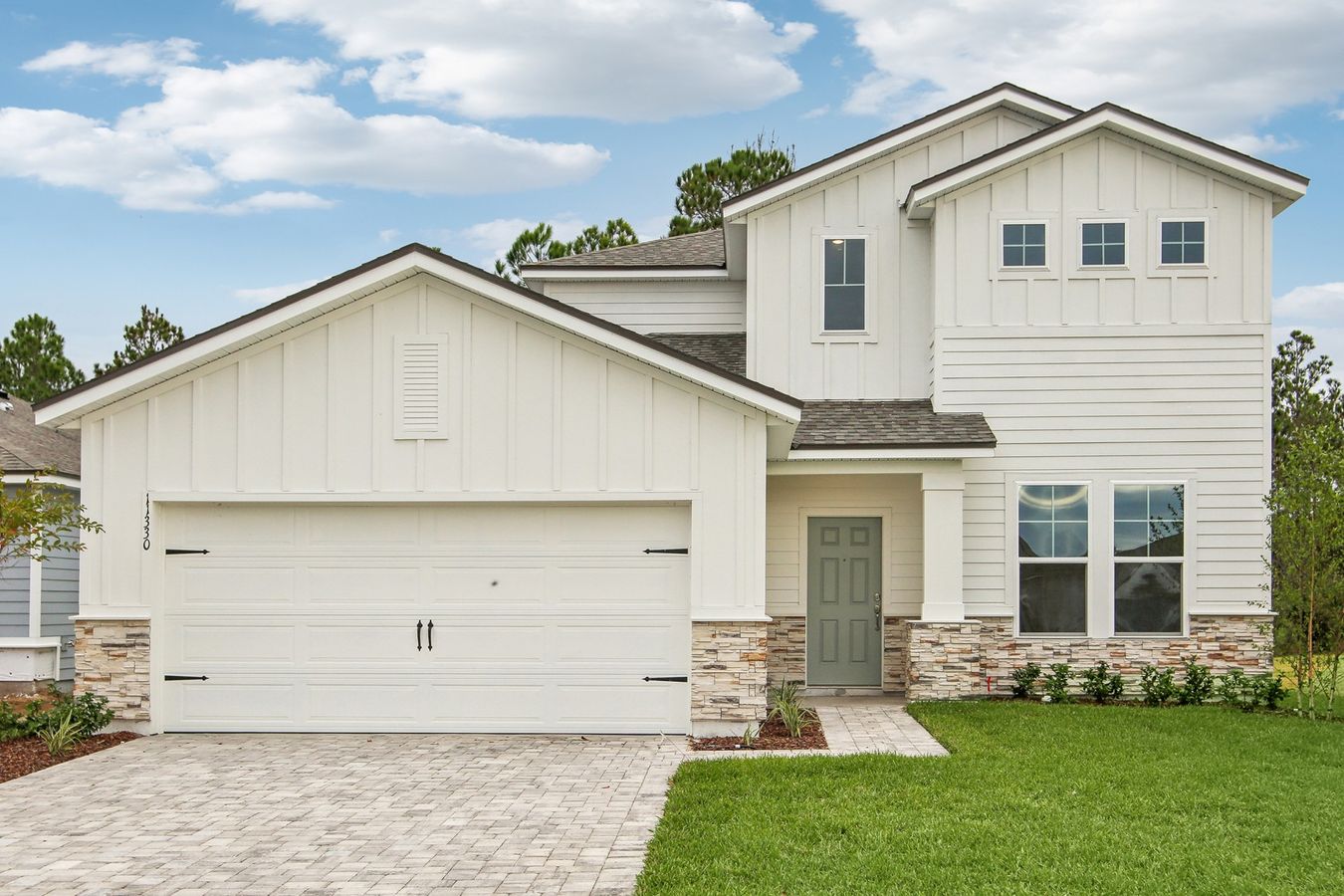 Sleek white siding and stone facade elevate this Panther Creek home, featuring expansive lawn and stylish entrance.