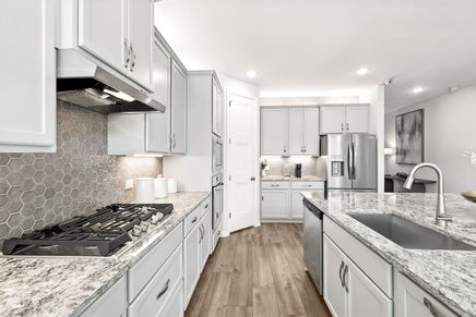 Exquisite white cabinetry, hexagonal backsplash, and luxurious granite countertops define this Green Oaks Preserve kitchen.