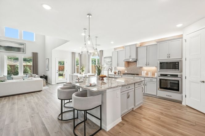 Opulent granite island, pristine gray cabinetry, and chic pendant lights in Green Oaks Preserve kitchen.