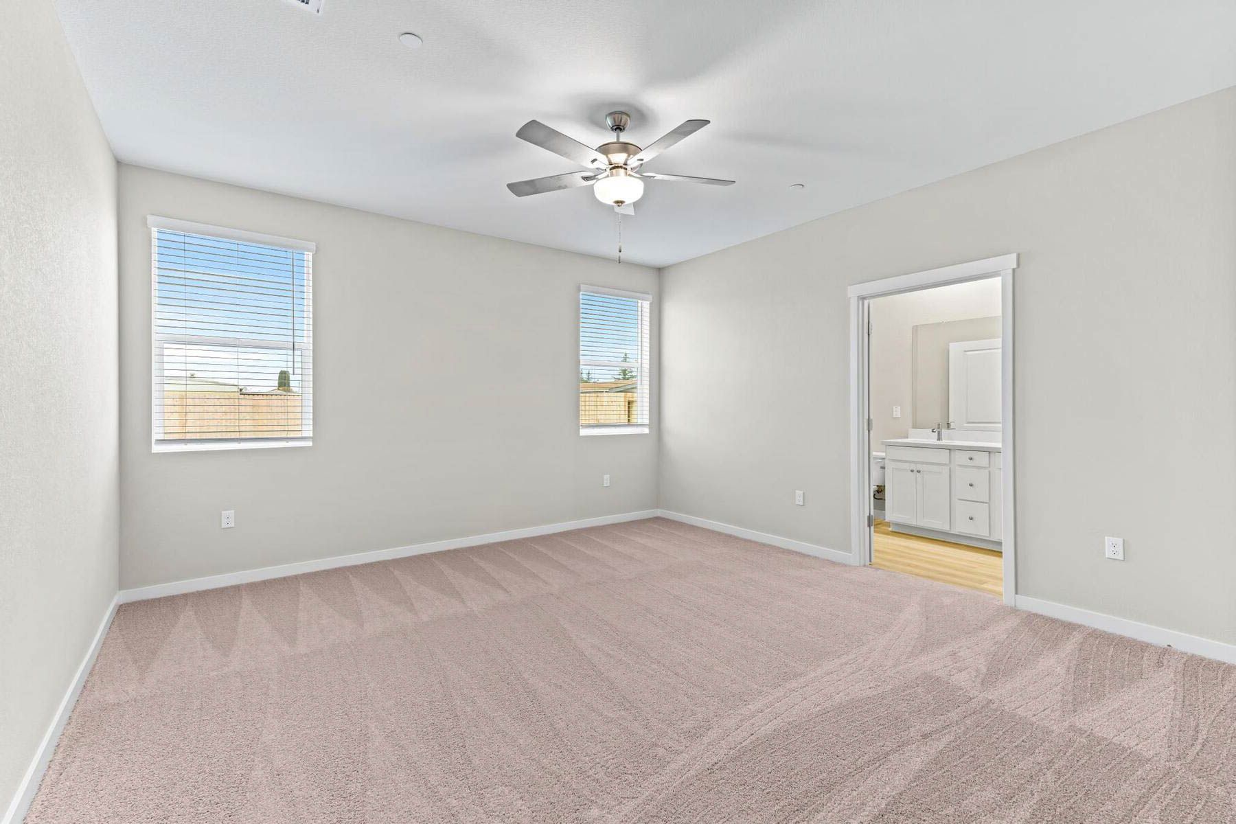 The master bedroom has two large windows and a ceiling fan.