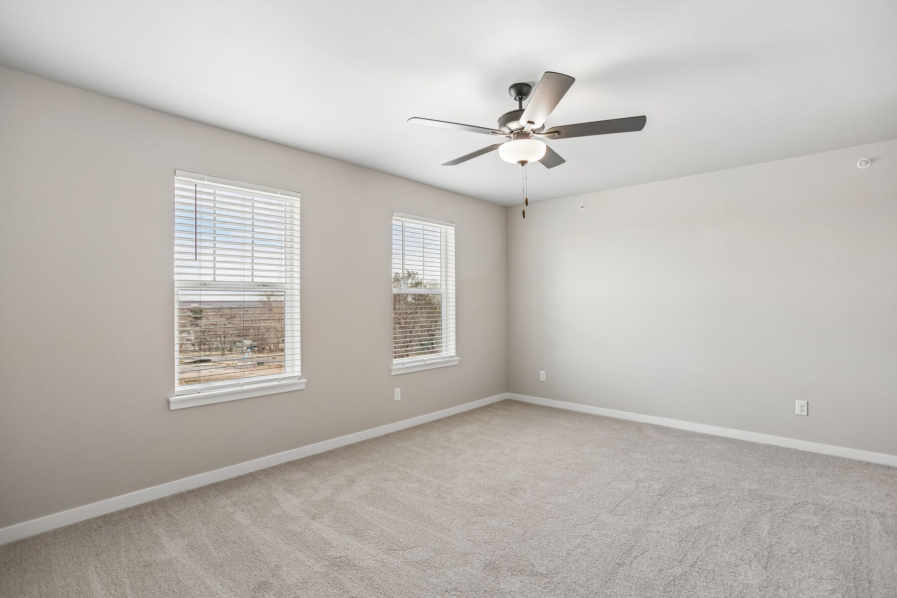 The master bedroom is spacious with windows and a ceiling fan.