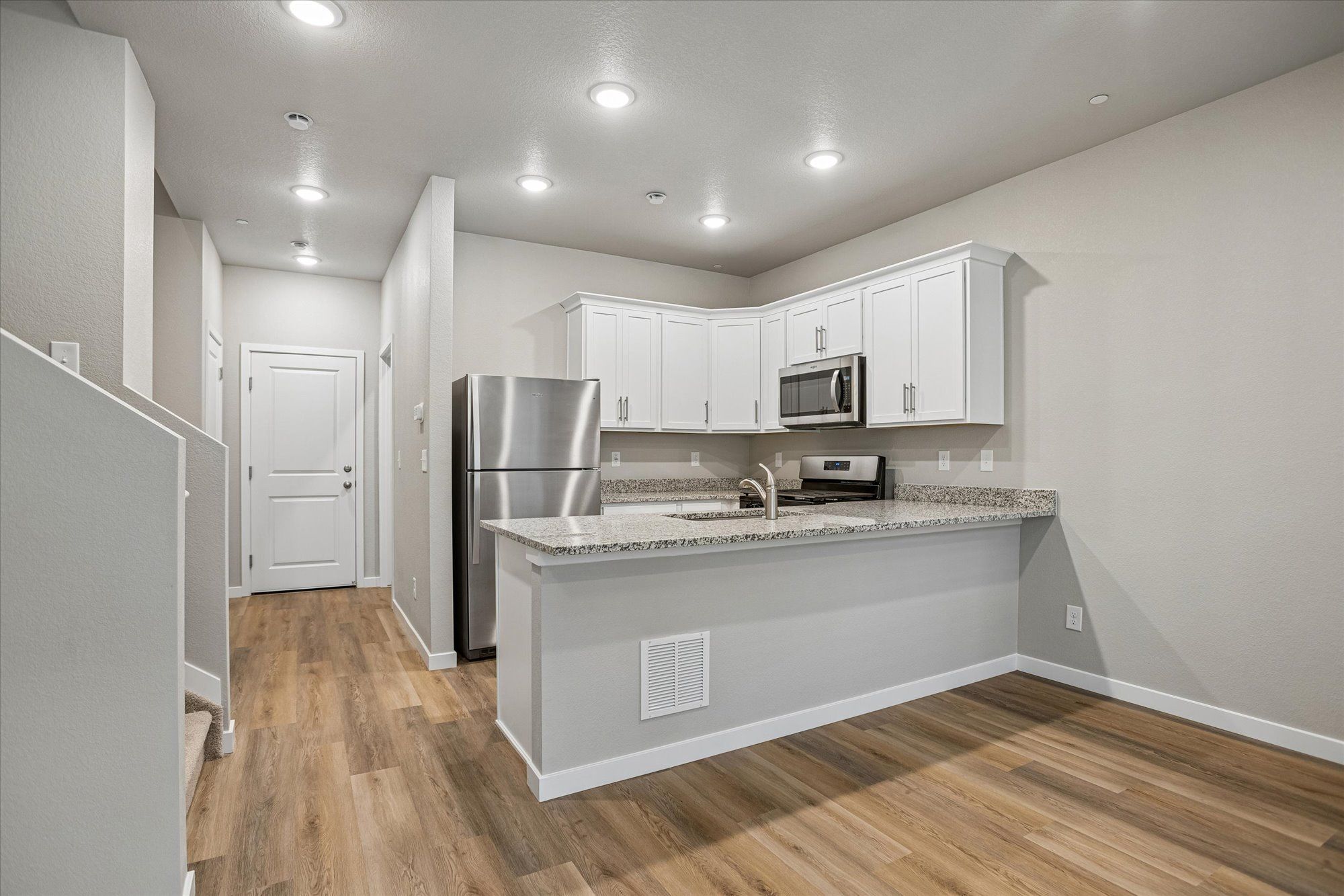 The kitchen has stainless steel appliances and plank flooring.