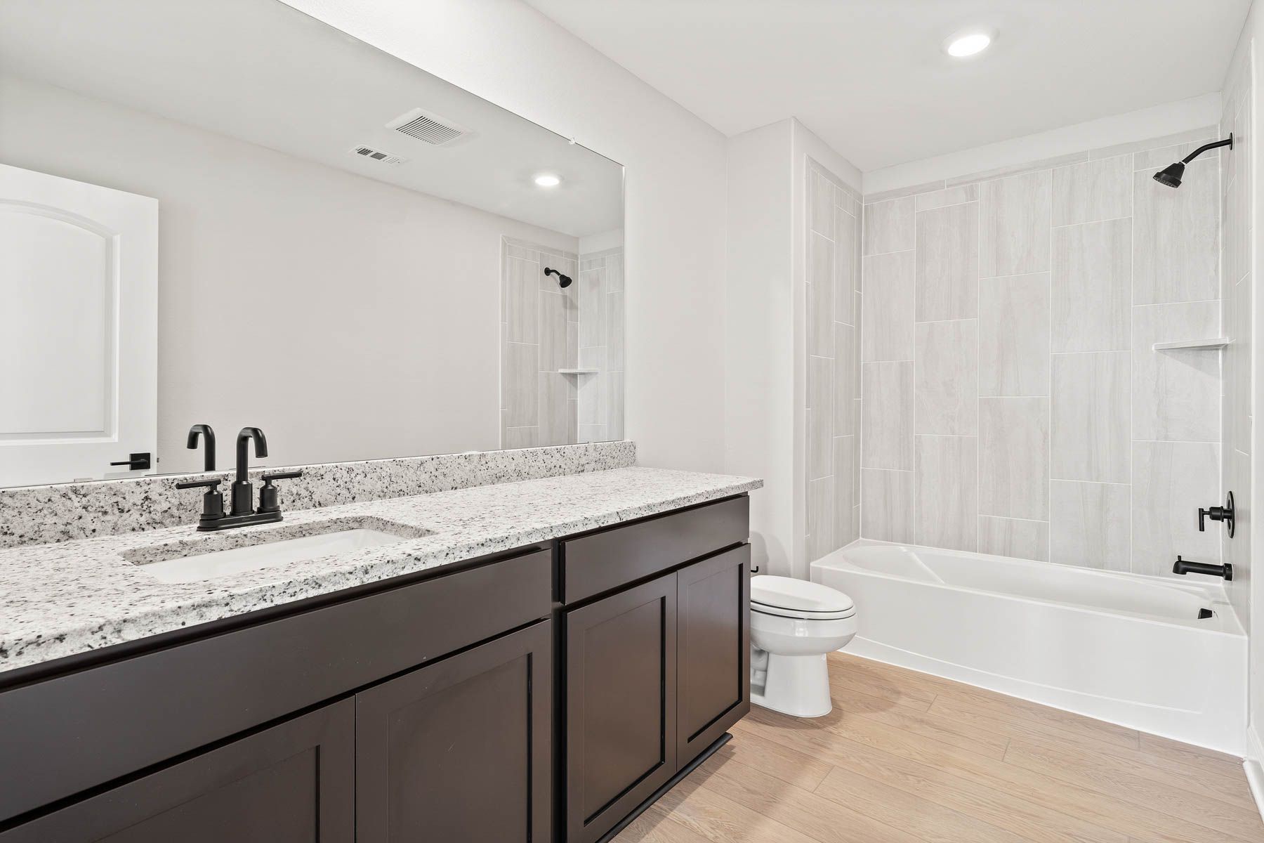 The secondary bathroom has a large vanity area and a beautiful tiled shower-tub combo. 