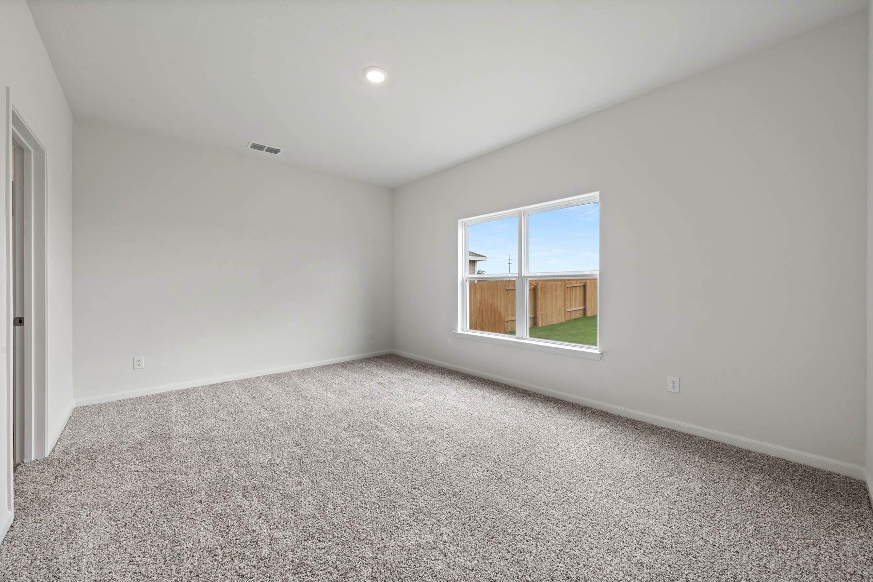 The large master bedroom of the Driftwood has a large window with backyard views.