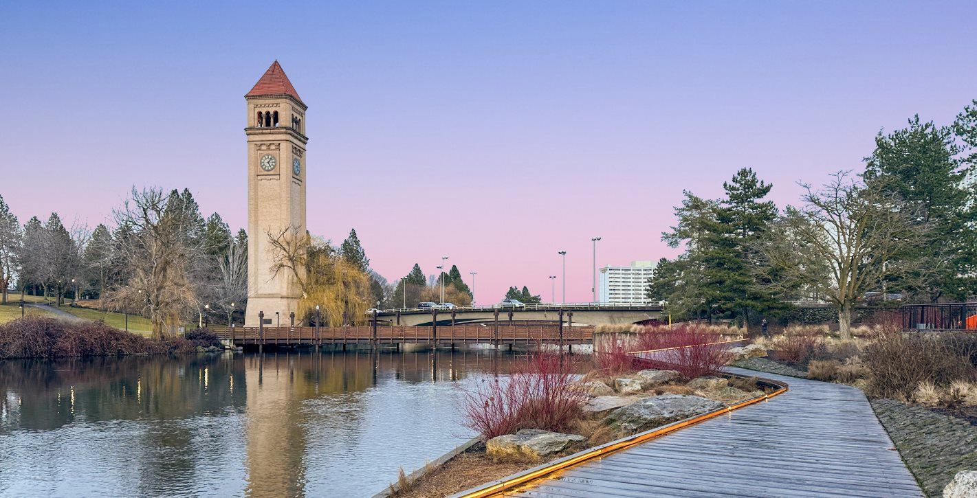The Riverfront walkway at dusk. The sky is a pink-purple hue and there is a walking path and a tall