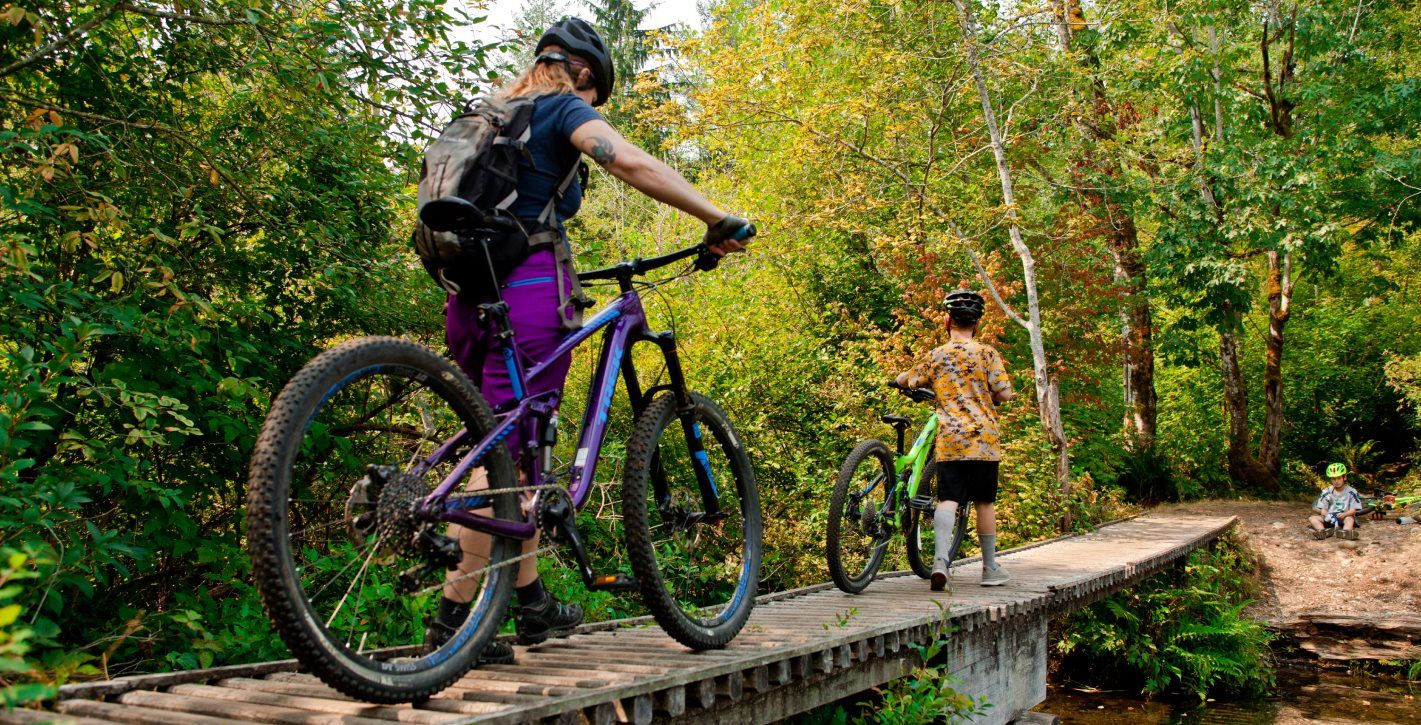 People walking their bikes across a bridge surrounded by greenery