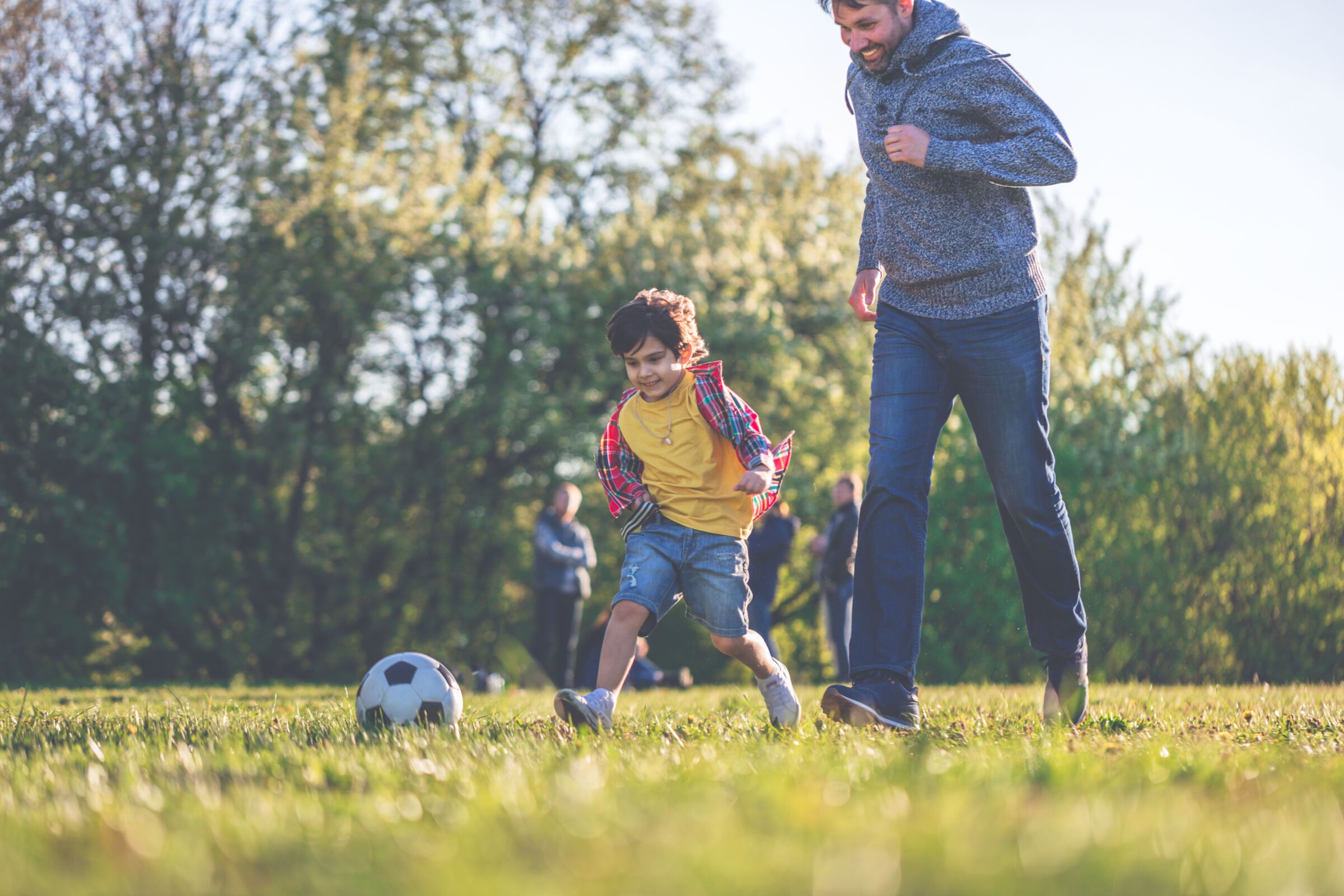 Father and son playing with a soccer play in a park on a sunny day.