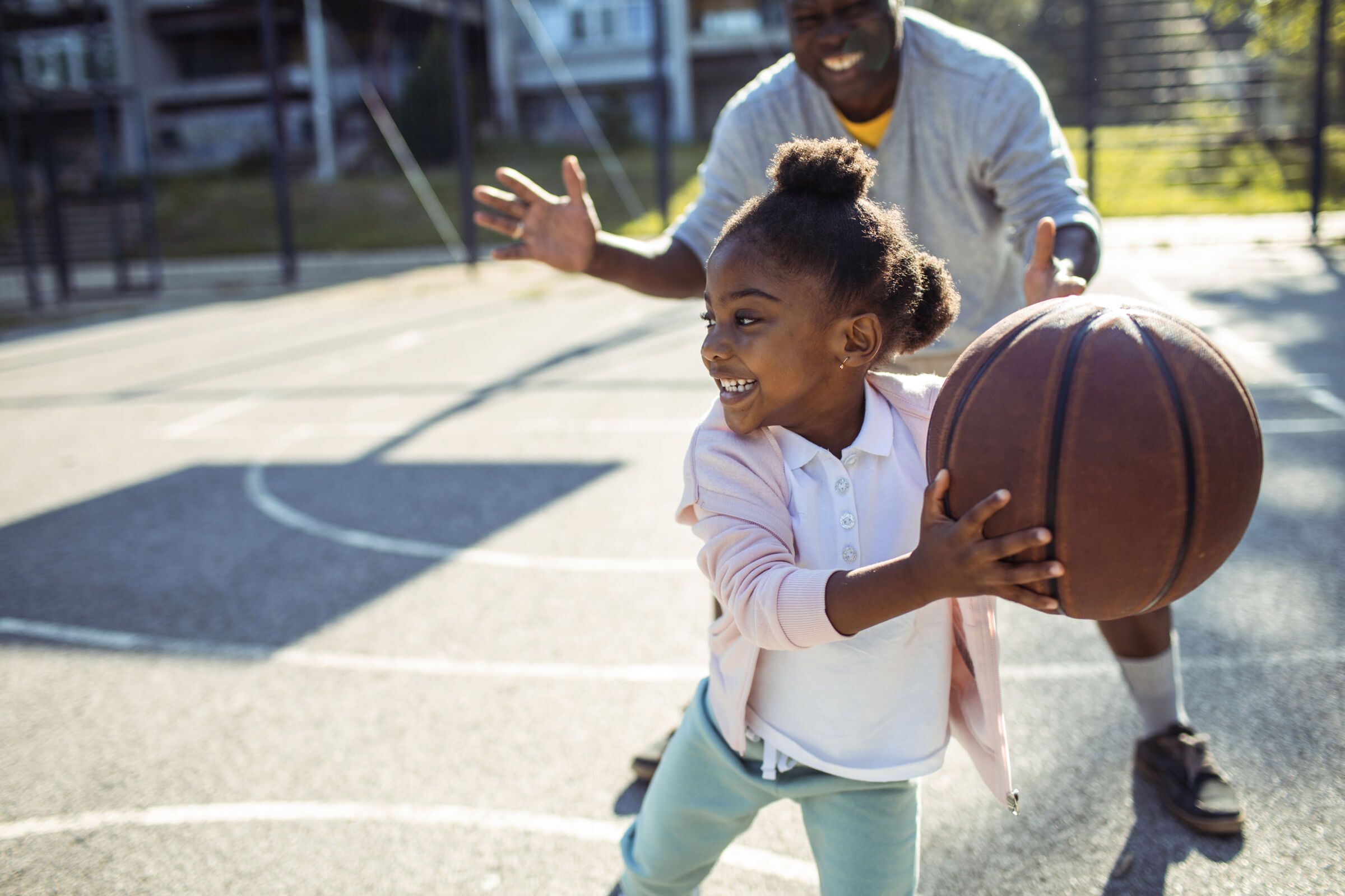 Father and daughter play basketball on a sunny day.