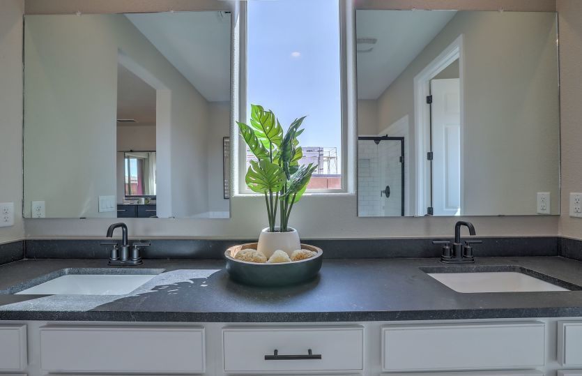 Owner's suite vanity including granite countertops, two sinks, lots of cabinet space, and a window f