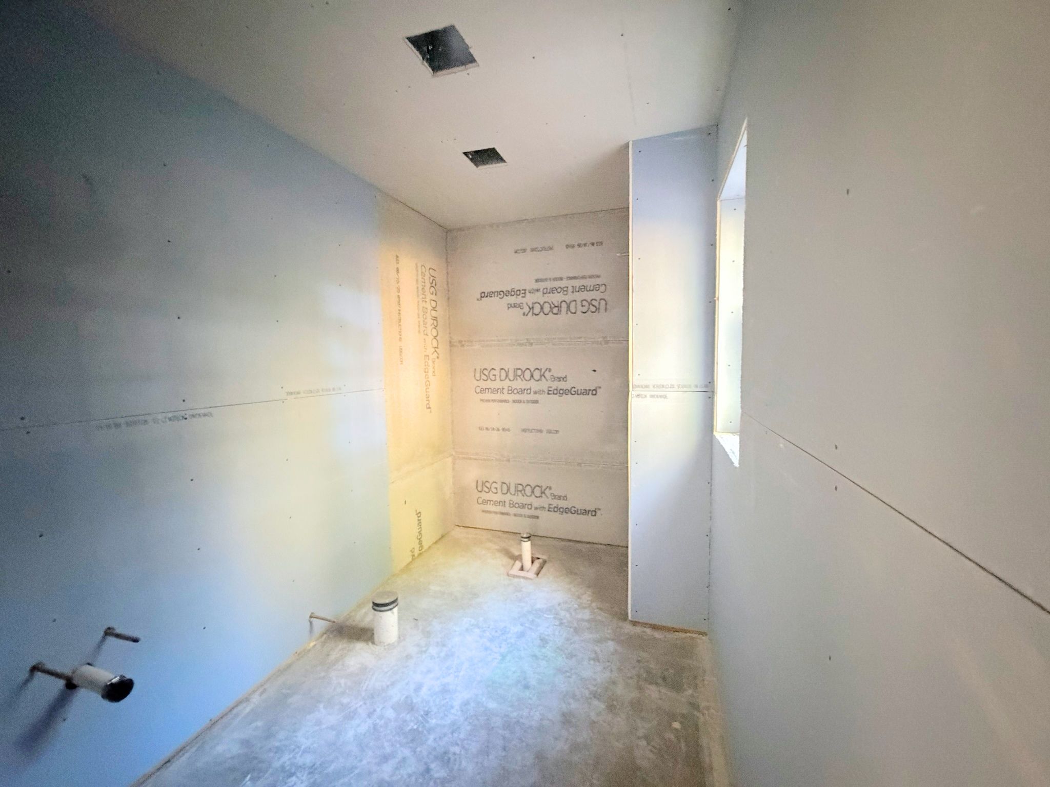 Bathroom construction progress view of wall preparation and plumbing related finish work progressing.