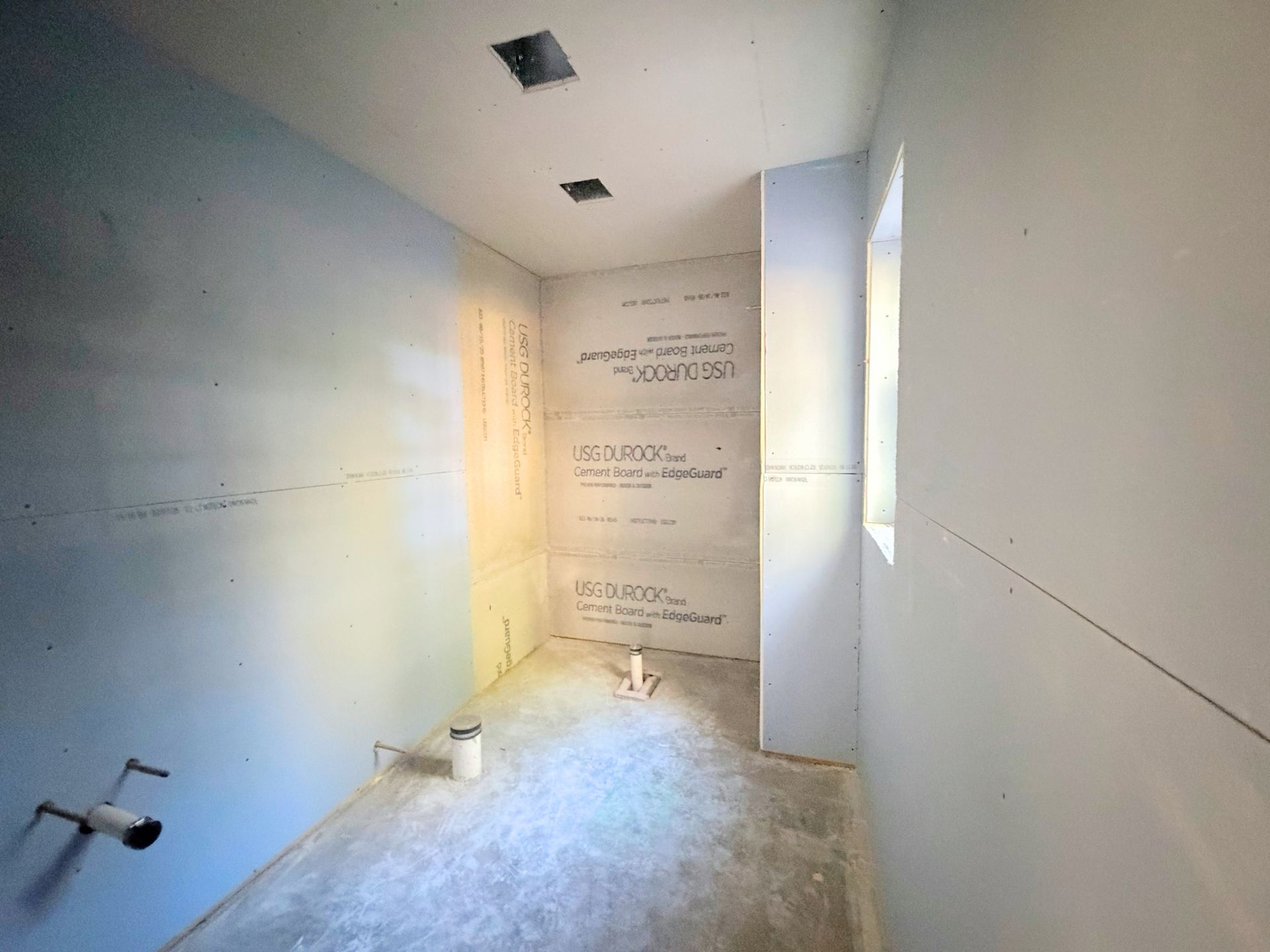 Bathroom construction progress view of wall preparation and plumbing related finish work progressing.