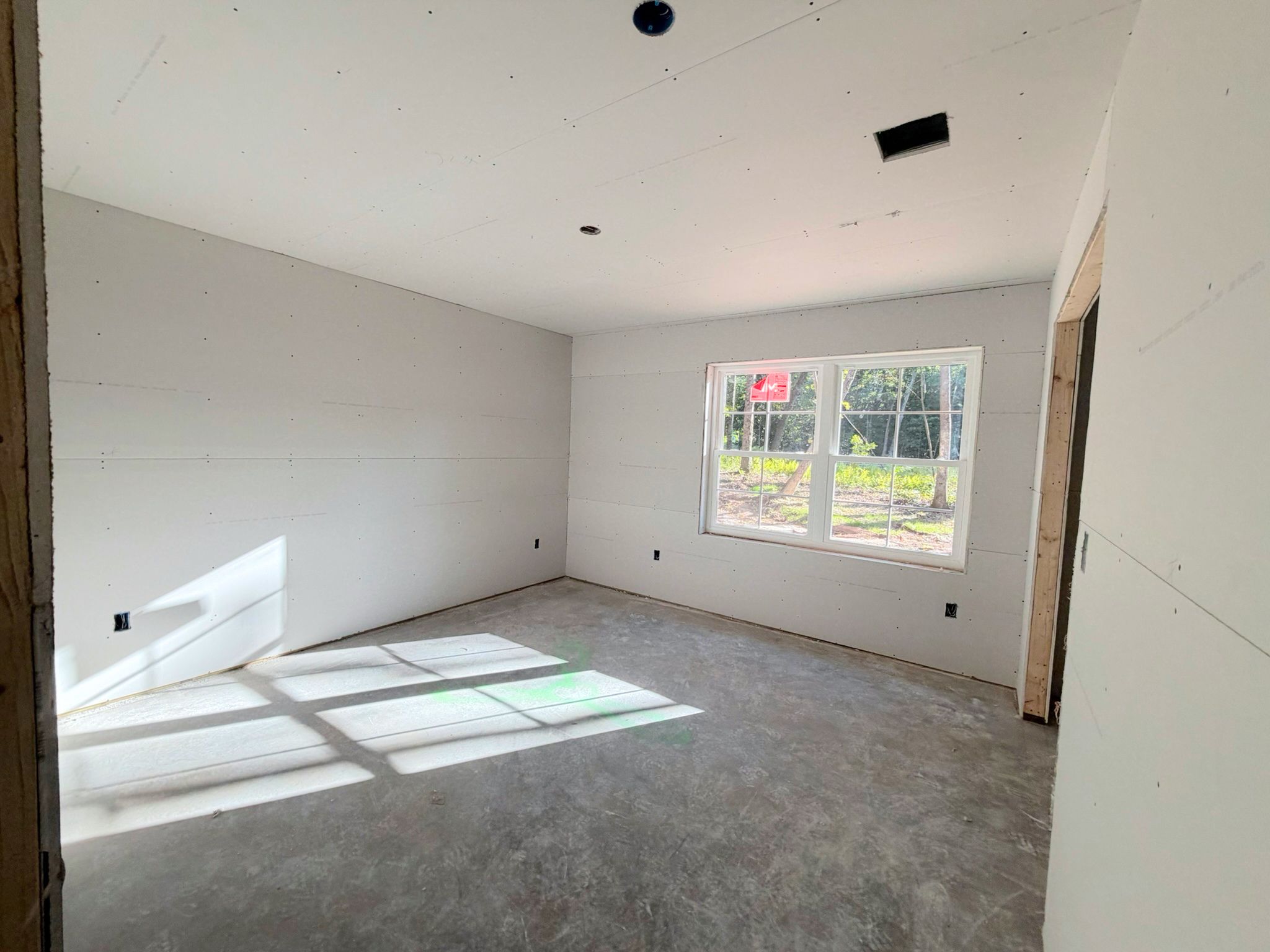 Progress photo of the sunlit lower level bedroom in progress with wall surfaces completed and finish work still underway.