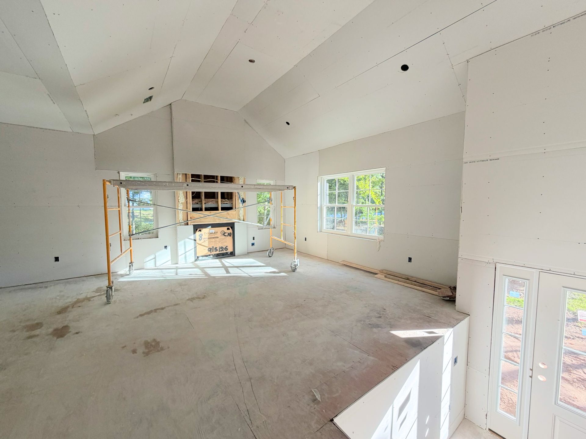 Bright living room under construction with drywall installed and natural light filling the space as fireplace installation begins.