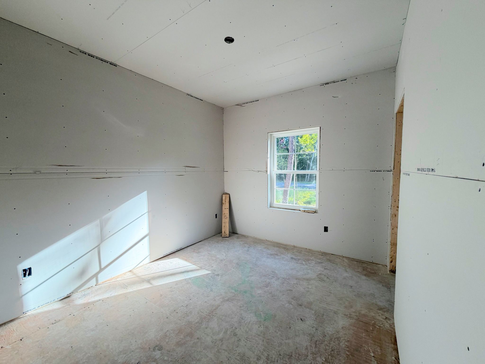 Bedroom construction view showing completed drywall, closet entry preparation and natural light filling the space.