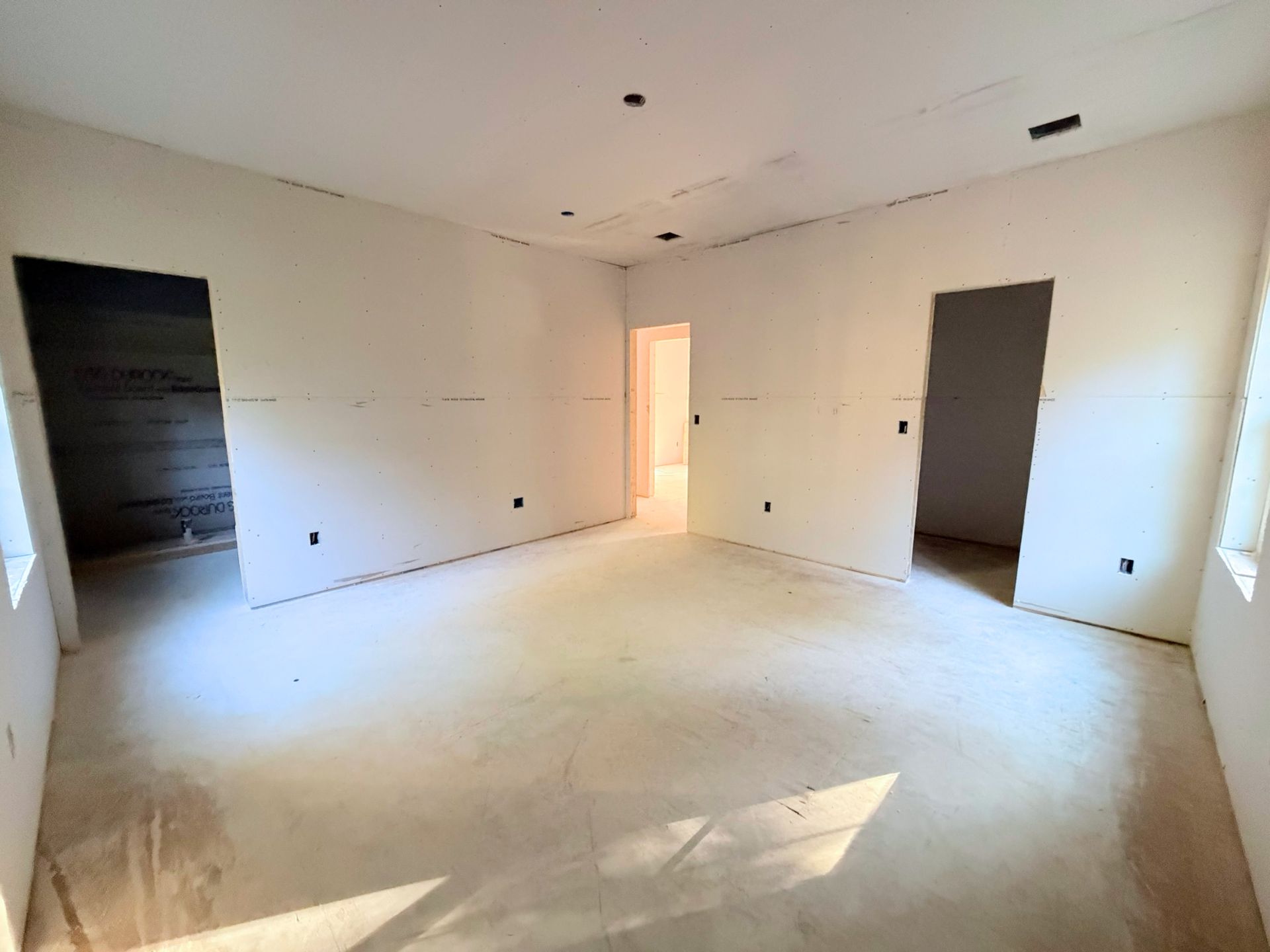Master bedroom interior area nearing the finish stage, with drywall completed and openings clearly defining the adjoining walk-in closet and master bath.
